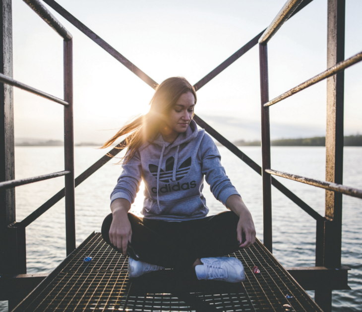 Jente som sitter på brygget ved havet i solnedgang